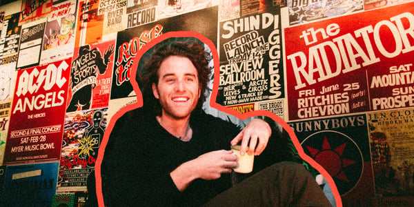 Matt Walters holding a mug and smiling against a background of Australian music posters